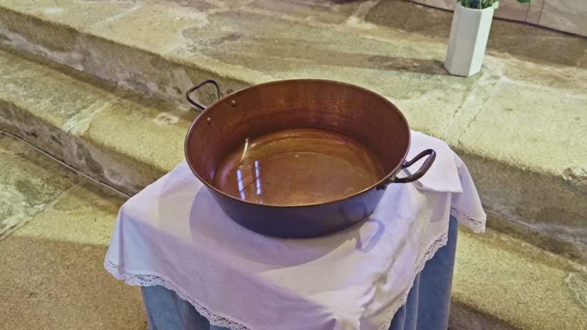 Slow push-in toward a baptismal font inside a church during a baptism ceremony.