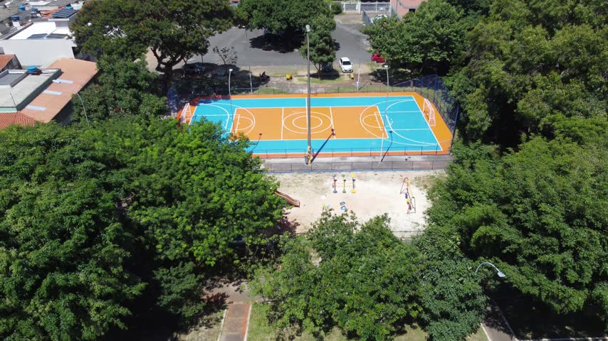 Aerial reveal, colorful community sports court in Brasilia, Brazil, surrounded by mature trees, residential buildings and sprawling urban neighborhoods