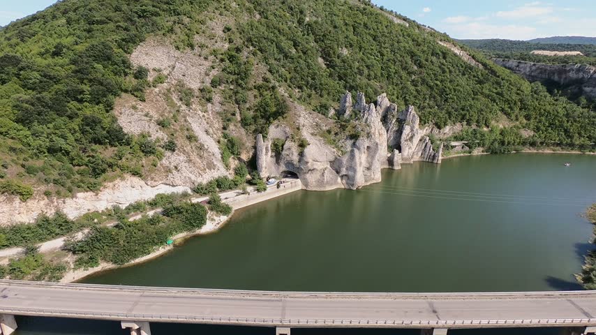 Aerial view of a concrete bridge crossing over a lake with cars driving by and the wonderful rocks natural phenomenon in the background, a popular tourist destination in bulgaria