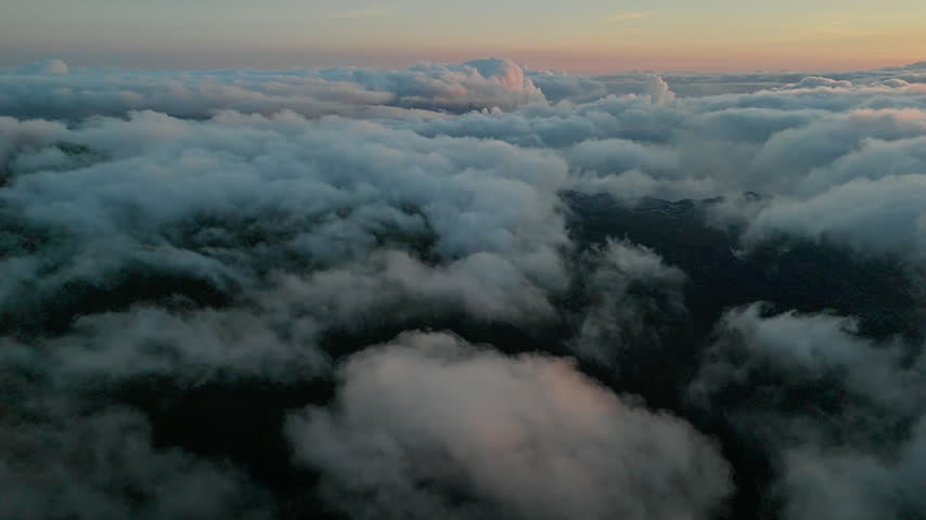 Layered clouds over dark mountain terrain beneath pink dawn sky. Transition from night to morning.