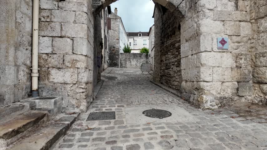 Stone arch entrance leads into the old center of Moret-sur-Loing along a narrow cobblestone passage.