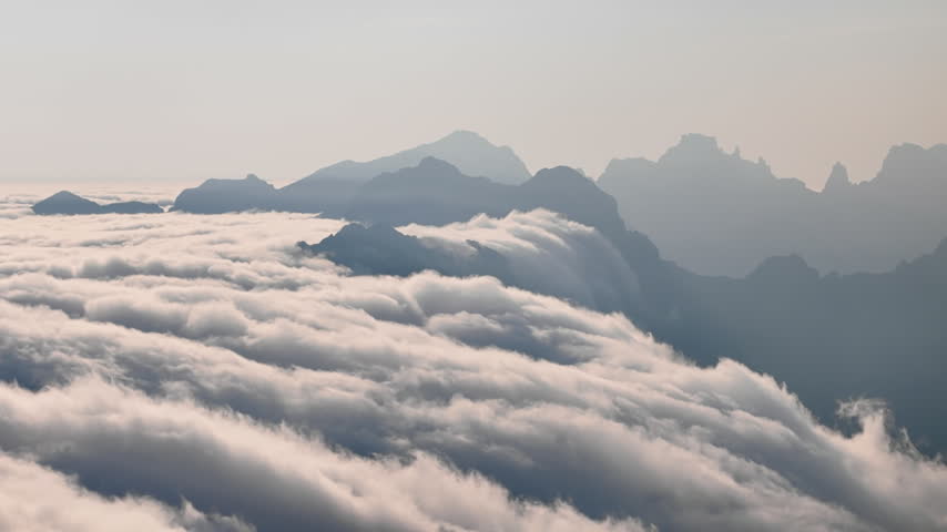 Mountain peaks above moving clouds. Aerial view of cloud cover around rocky ridges