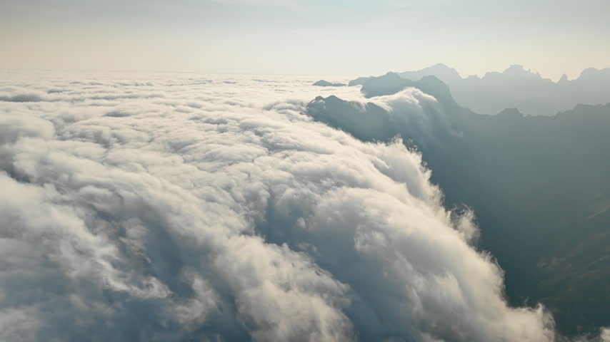 Clouds moving along mountain ridge above valley. Aerial view from above dense cloud layer.