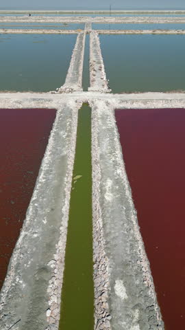 High angle aerial shot showing geometric salt evaporation ponds with vibrant red and green water colors. Suitable for environmental, sustainability, and industrial geography projects.