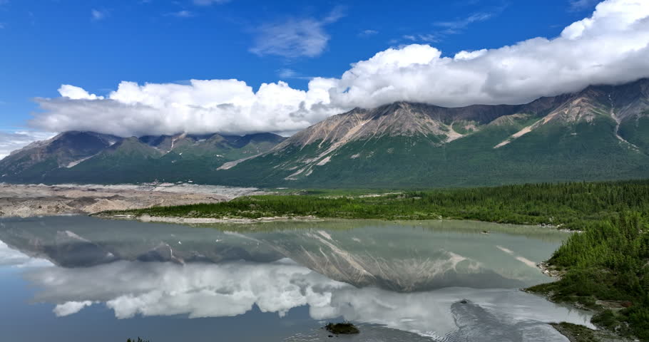 Mountains covered with fluffy clouds reflect in the waterscape. Beautiful nature of Alaska, USA. Aerial view.