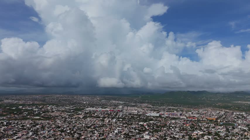 Wide aerial view of Cabo San Lucas city showing green mountains and massive storm clouds building in the background; Baja California Sur, Mexico.