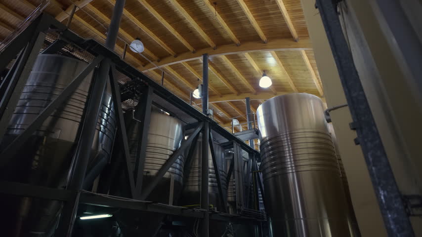 Camera tracks across large stainless steel wine fermentation tanks inside a commercial winery facility in Argentina.