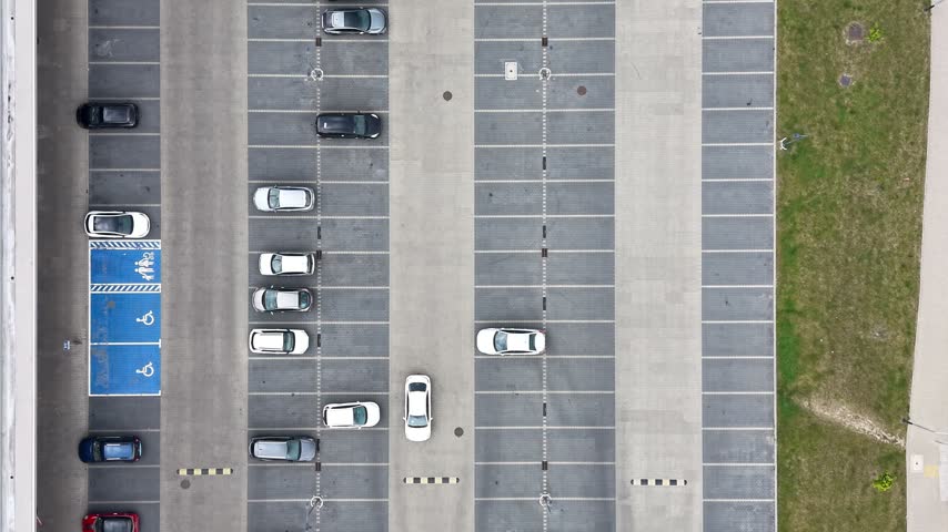 Aerial view of a busy shopping mall parking lot showing cars parked in designated spaces, with blue handicapped spots and a crosswalk visible in the foreground