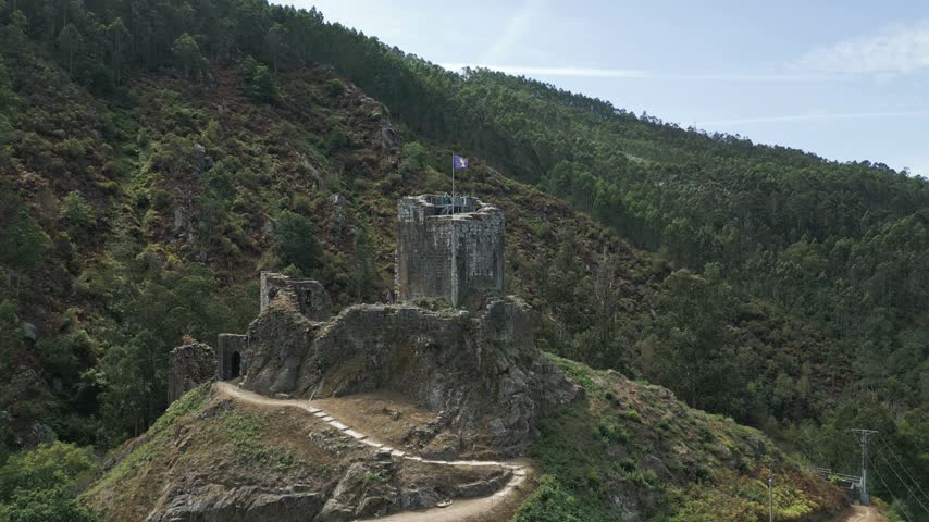 Majestic ruins of the medieval Naraio Castle standing on a rocky hill surrounded by a lush green forest in Galicia, a historical region in the northwest of Spain, on a sunny summer day