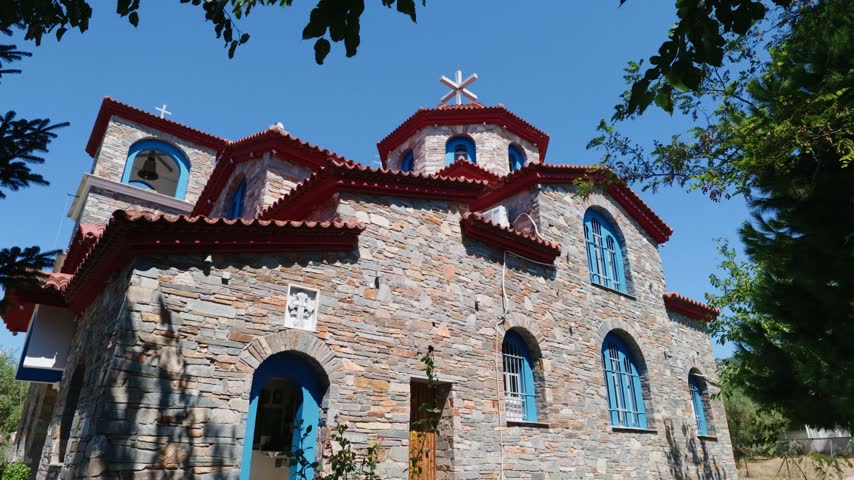 Exterior view of a traditional Greek Orthodox church in Thassos, Greece, with stone walls, red roof details and Mediterranean surroundings.