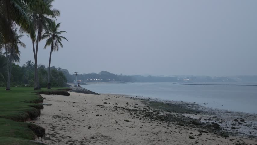 A peaceful landscape showcasing a scenic public park alongside a sandy beach and a flowing river under hazy skies.