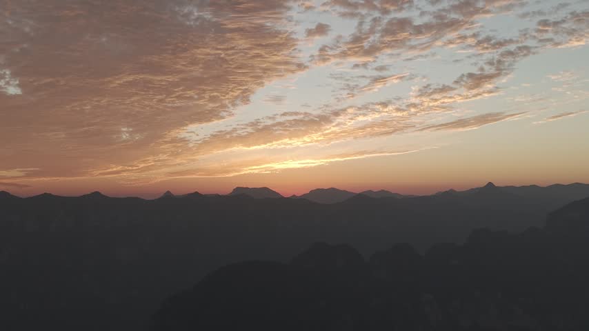 Aerial view of a vibrant autumn sunset over Taihang Mountains, China. Dramatic pink and orange textured clouds fill the sky above dark silhouettes of Wanxian peaks.