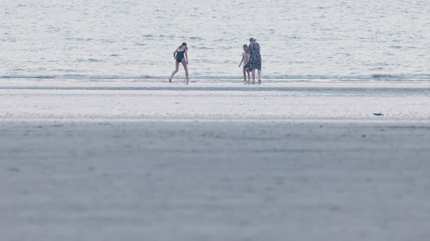 Family standing in shallow sea girl boy and woman is talking on the phone