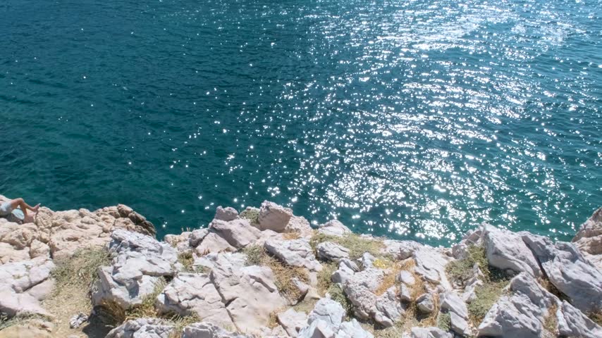 Sunlight sparkles across the sea as waves crash against the rugged rocks of Les Goudes