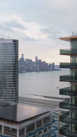 Vertical video: Modern skyscrapers and residential buildings along the Hudson River in Jersey City, New Jersey, with Lower Manhattan in the background