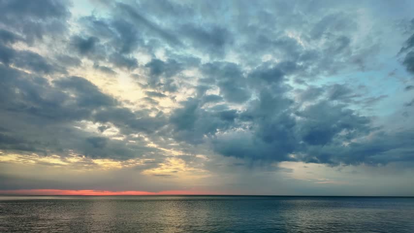 Dramatic clouds over a calm sea with a red sunset glow on the horizon.