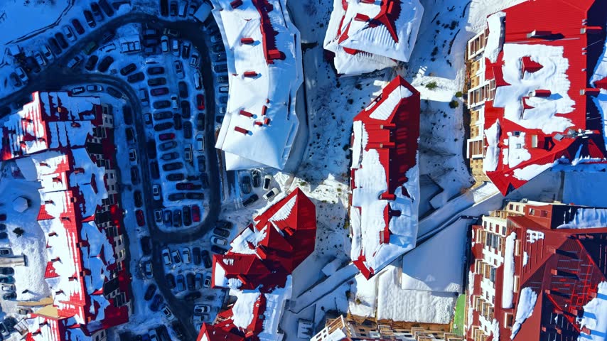 Telecommunication tower on a mountain peak under blue sky. Aerial shot shows a tall red and white antenna structure above dark forested hills.