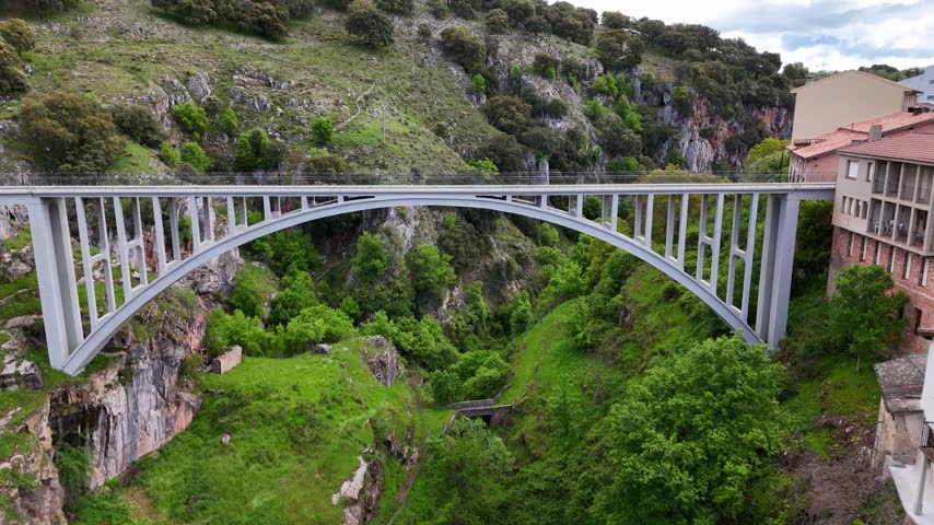 Aerial view of large concrete arch bridge over canyon and mountain village