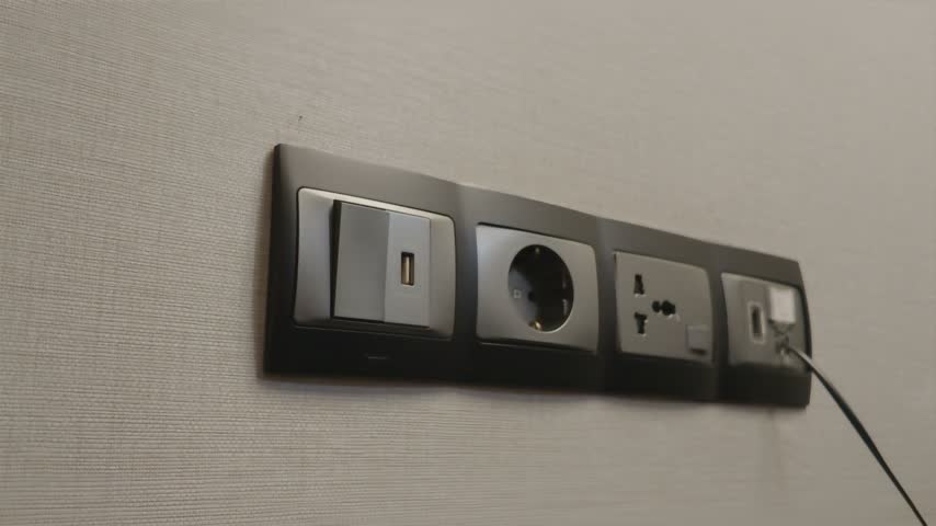 Male hand reaching towards a modern multi socket electrical outlet panel on the wall.