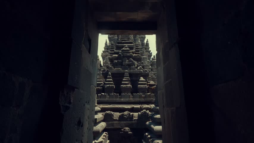 A static view looking out from a dark interior room through a rectangular door frame, focusing on the intricate stone platforms, base, and steps of the temple structure directly ahead.