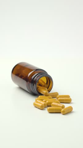Yellow Pills Spilling From Amber Glass Medicine Bottle in Vertical View 