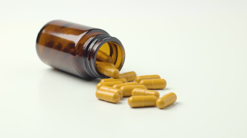 Yellow Pills Spilling From Amber Glass Medicine Bottle with Slow Rotating View