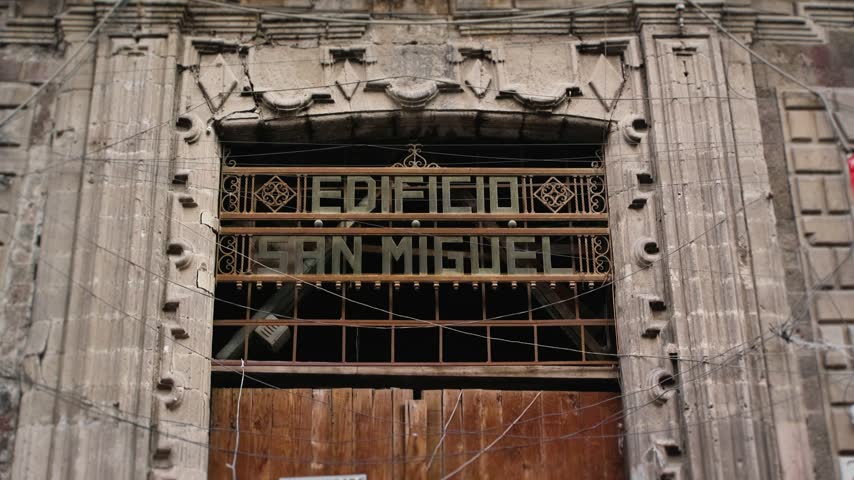 Close close up of ornate stone facade and metal sign reading EDIFICIO SAN MIGUEL above a boarded entrance in Mexico Citys historic center