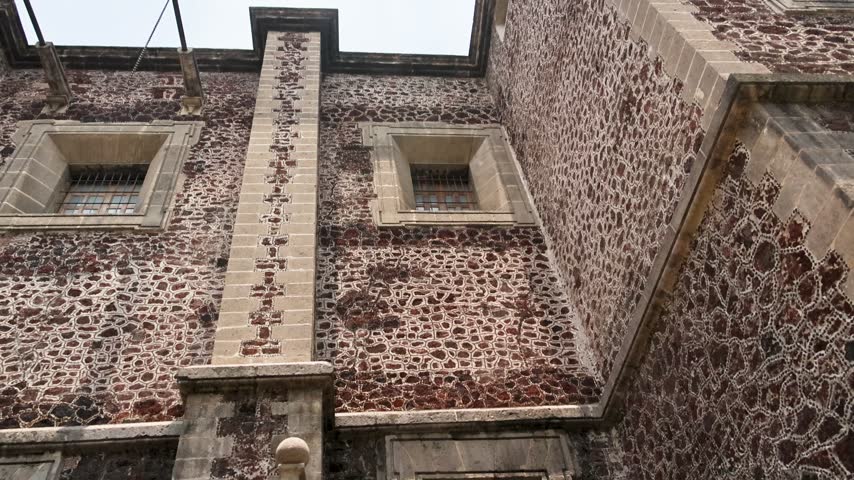 Historic National Palace facade in Mexico City Zocalo built with red porous volcanic tezontle stone framed by pale masonry, shown in upward view
