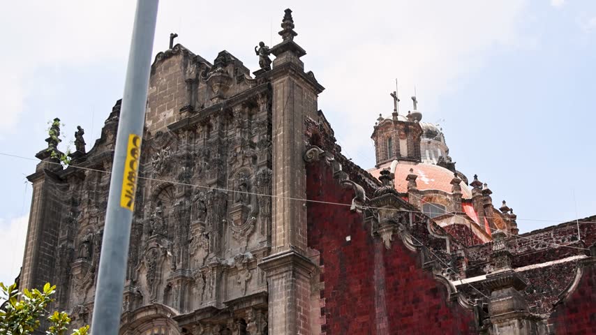 Facade of Santo Domingo church in Mexico City historic center showing red tezontle volcanic stone and cantera architectural elements.