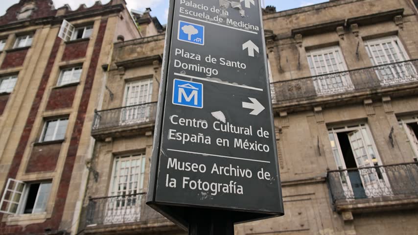A wayfinding street sign directs pedestrians to Santo Domingo Plaza, cultural centers, and a photography museum in Mexico City.