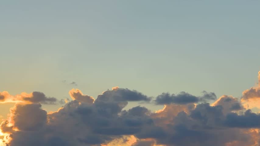 Dark, dramatic clouds moving across a beautiful orange, yellow, and blue sky during sunset