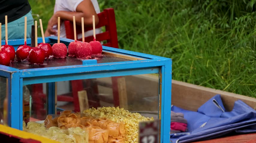 Bright red candy apples and bags of popcorn displayed on a blue glass cart offered by a vendor in Xochimilco Mexico City.