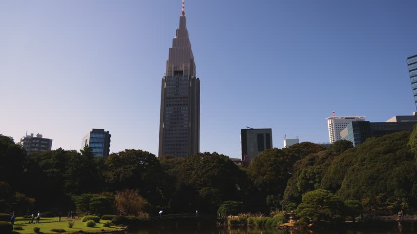Shinjuku Gyoen National Garden in Naitomachi, Shinjuku and Shibuya, Tokyo, Kanto Region, Honshu Island, Japan, with pine trees, traditional Japanese landscape and city skyline behind on a sunny day