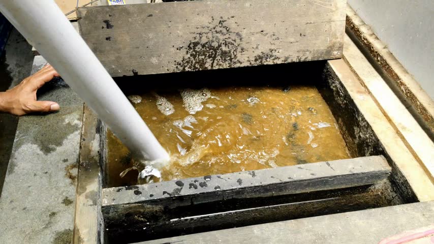 Close up shot of a person using a pipe tool to stir and clean murky water in a concrete fish pond.
