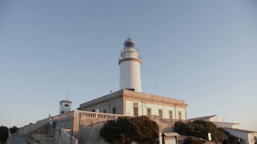 Formentor lighthouse, a white tower rising from the stone keepers house above a balustrade terrace in warm morning sun, static low angle, Cap de Formentor, Mallorca, Balearic Islands, Spain