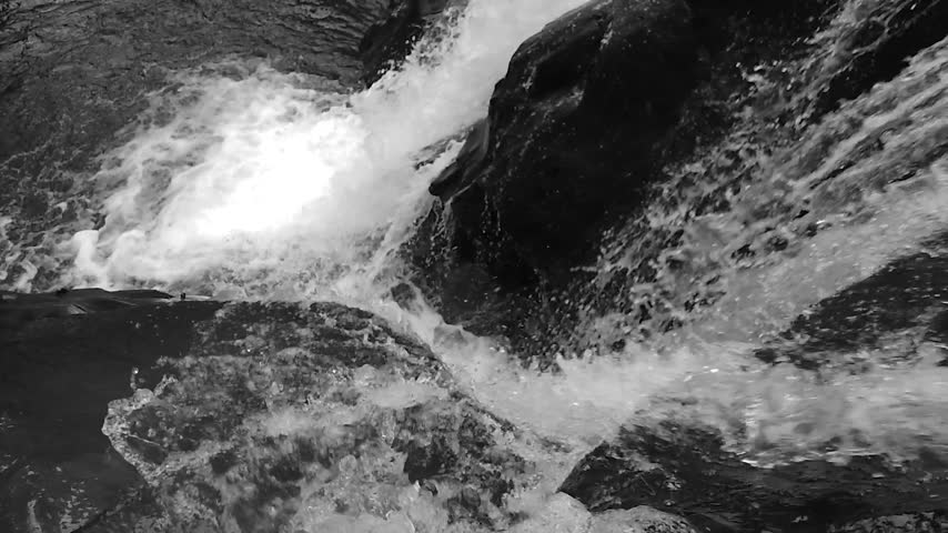 Black and white high angle close up of powerful waterfall rushing over rocks