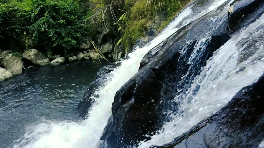 Rushing waterfall cascading down dark rocky slope into freshwater river pool