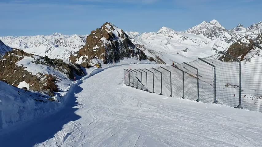 A ski trail descends between rocky mountain peaks and snow-covered slopes.