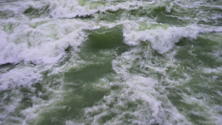 A Close-up View of Turbulent River Rapids with White Foam and Greenish Water. High quality 4k footageA dynamic close-up shot captures the powerful motion of churning river water filled with white foam