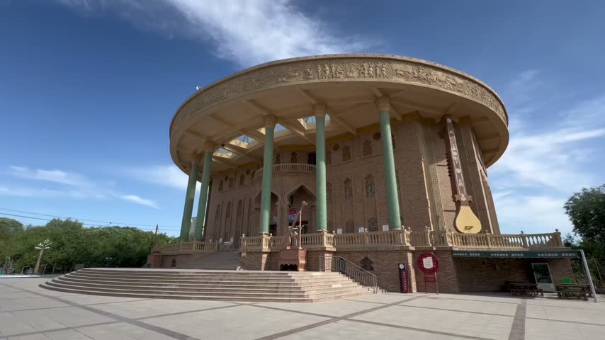 A massive circular building featuring ornate gold friezes and towering green columns stands under a clear blue sky.