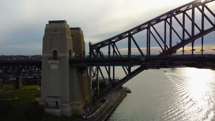 Famous sydney harbour bridge arch silhouetted against a cloudy sunset sky. Calm water of the harbour reflects the bright sunlight