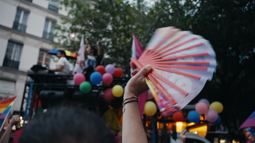 Person waving a colorful hand fan in the crowd during an outdoor lgbtq pride parade celebration