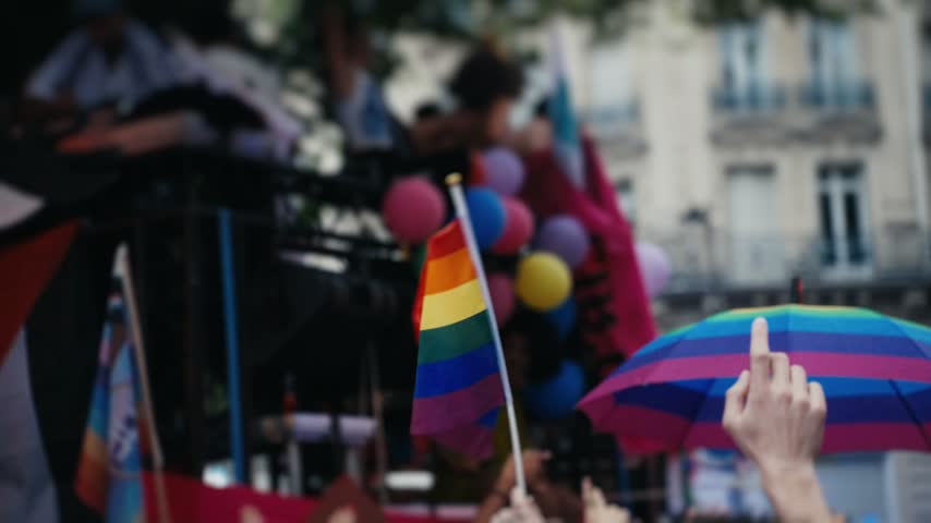 Colorful rainbow lgbtqia+ pride flag and umbrella waving in a crowded street during a pride parade
