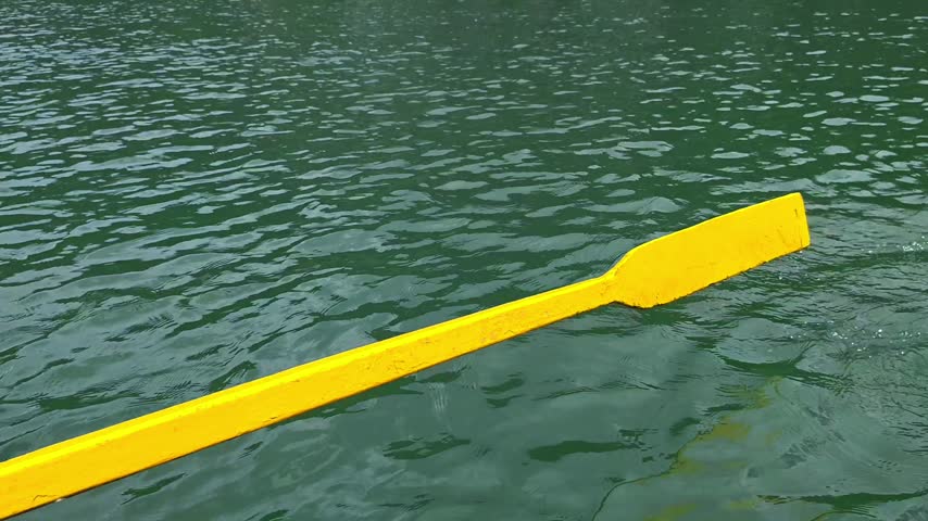 Yellow wooden oar rowing and splashing in clear green water