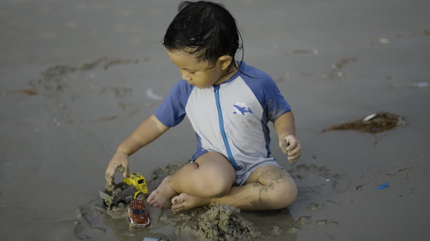 Little Boy Playing On Sandy Beach Near Ocean Waves. Young child having fun with sand toys at the seaside during summer day, suitable for family vacation promos or parenting lifestyle content.