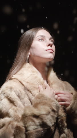 Young woman in fur coat under falling snow