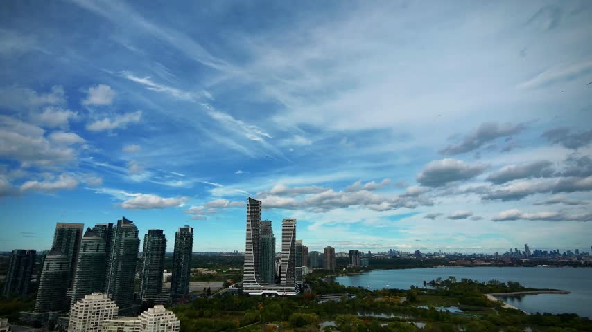 Tilt-Down Aerial From Condo Skyline to Marina Sailboats, Humber Bay. Opens on the Humber Bay condo skyline under a partly cloudy sky, then tilts down and descends into the marina basin — rows of docked sailboats, a small lighthouse, kayakers, and autumn trees.