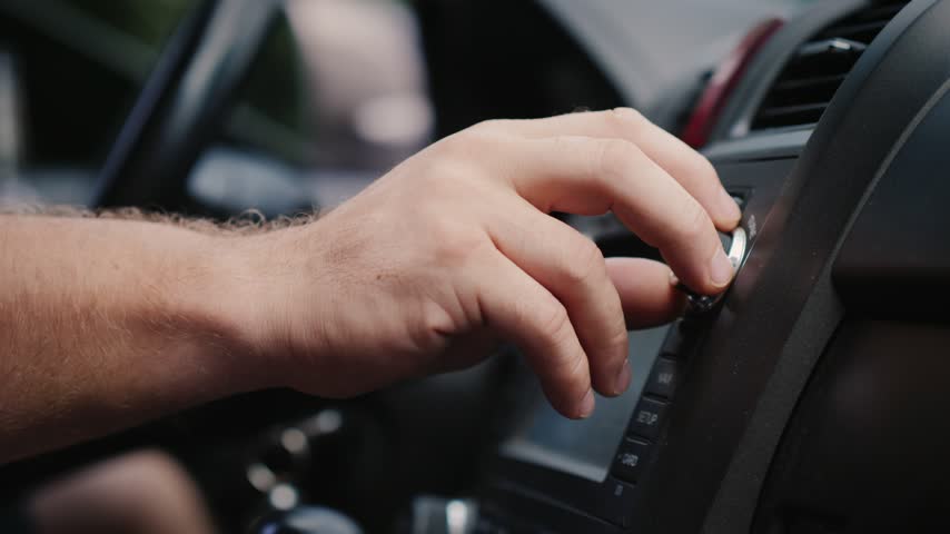 Close up shot of hand operating car stereo system, rotating volume knob and pressing buttons on console while driving, cinematic footage capturing vehicle technology and modern car interior.