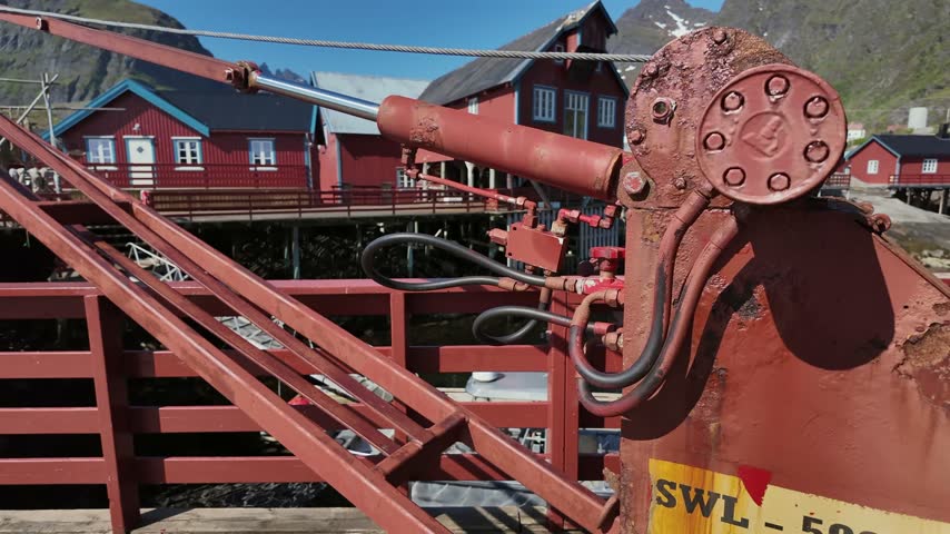 Red mechanical arm lowering to reveal the picturesque fishing village of A in the Lofoten Islands, Norway, on a bright sunny day