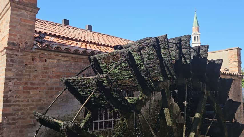 Historic Moss-Covered Water Wheel and Brick Mill With Bell Tower Under Clear Blue Sky